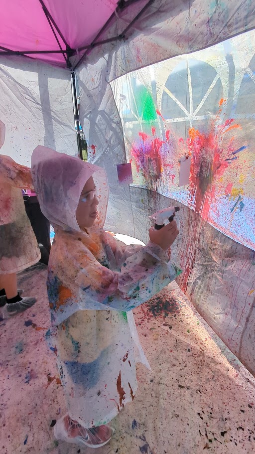 Young creator making colorful splatter art inside the paint tent