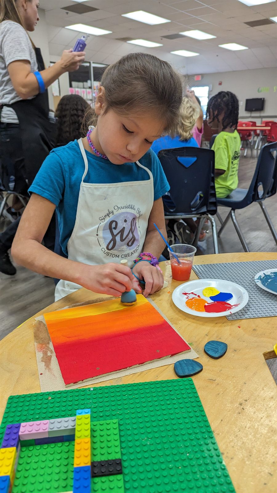 Child wearing a SIS apron painting a colorful project during a group event